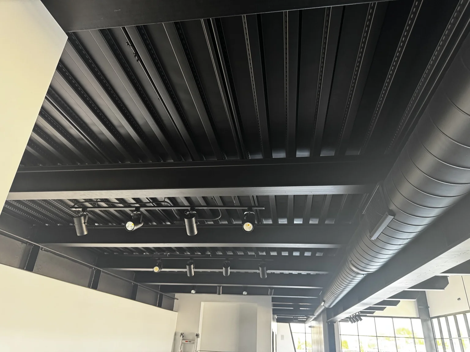 Boat-shop showroom ceiling finished in black with exposed beams, decking, ductwork, and track lighting