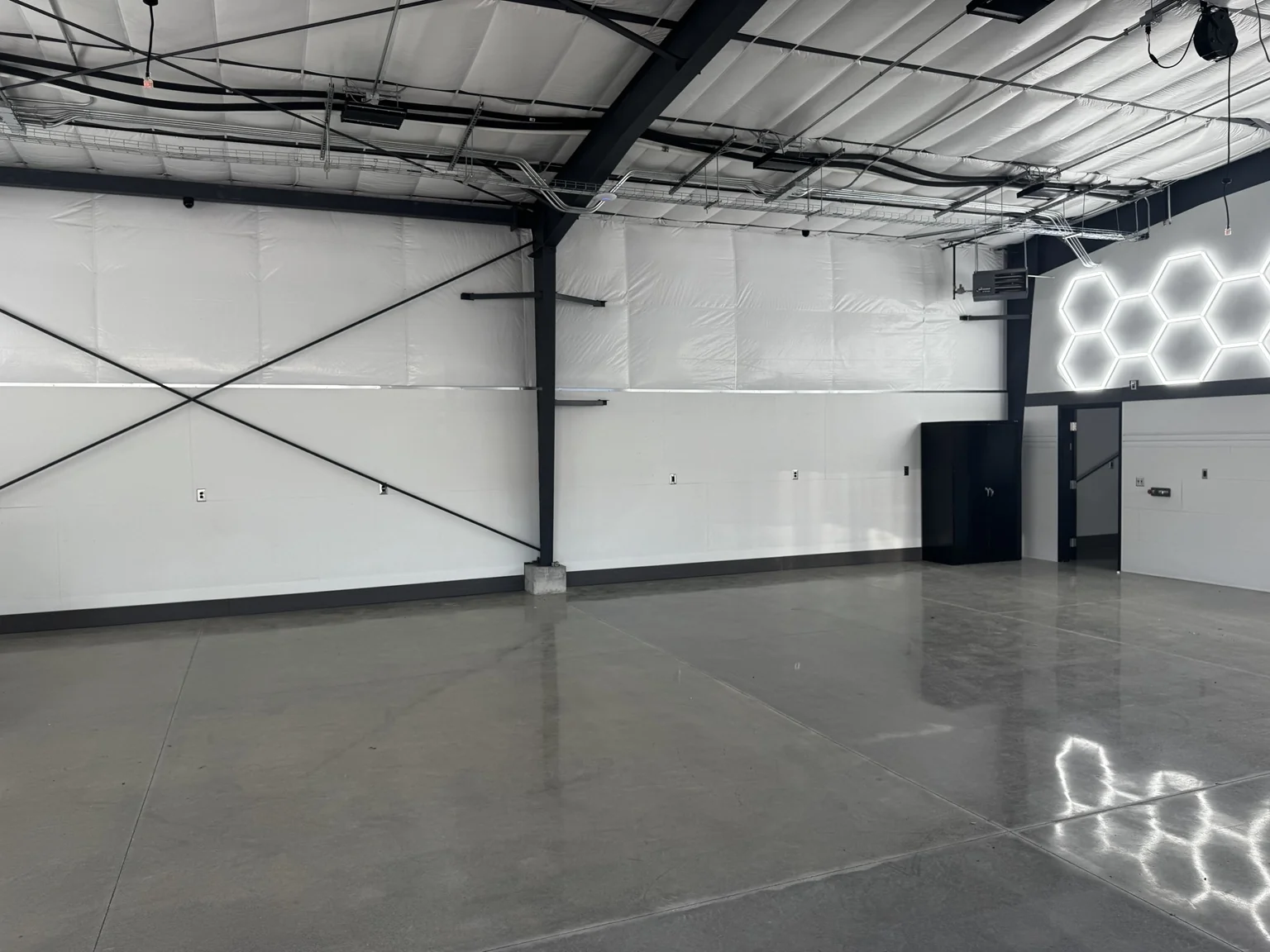 Finished boat-shop service bay with a polished reflective floor, white walls, black steel framing, and illuminated hexagon wall feature