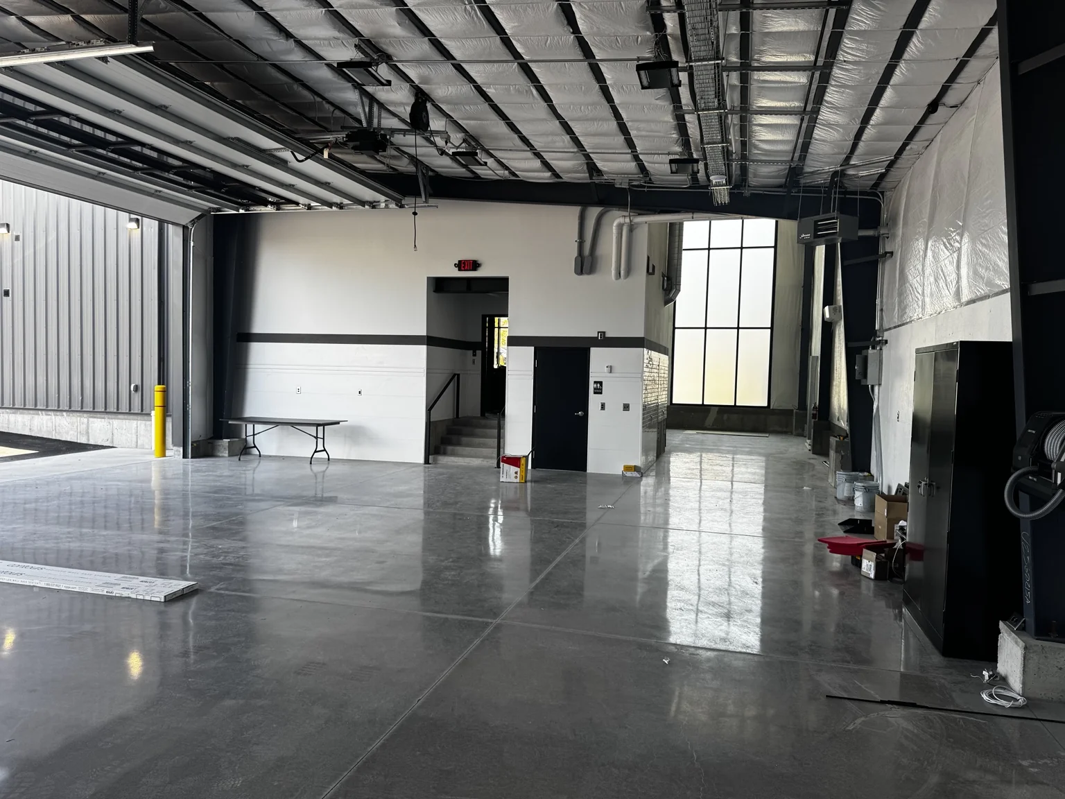 Large finished boat-shop service area with reflective concrete flooring, white walls, and black structural framing