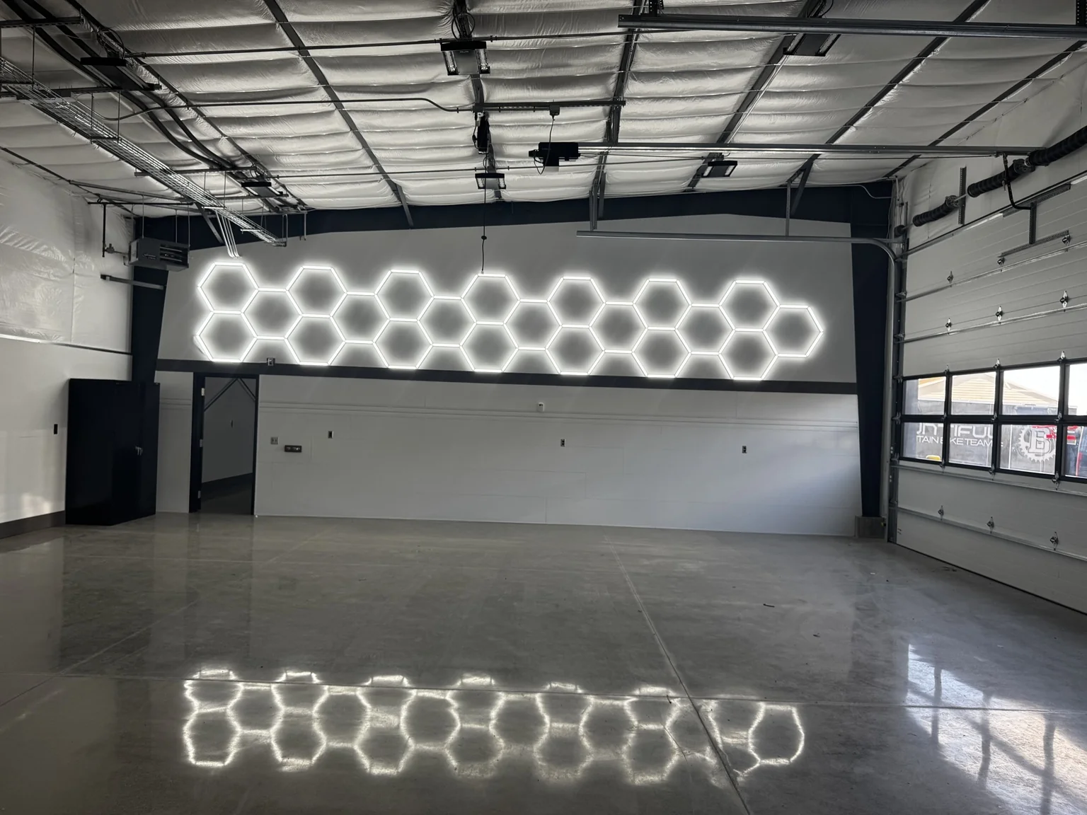 Boat-shop interior featuring a long illuminated hexagon wall installation reflected across the polished floor