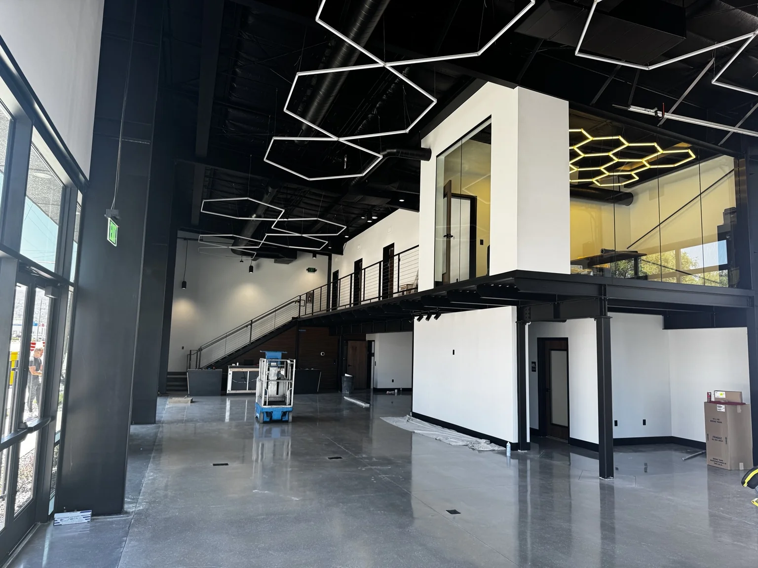 Completed boat-shop showroom featuring a polished concrete floor, black steel mezzanine, white office walls, and suspended geometric lighting