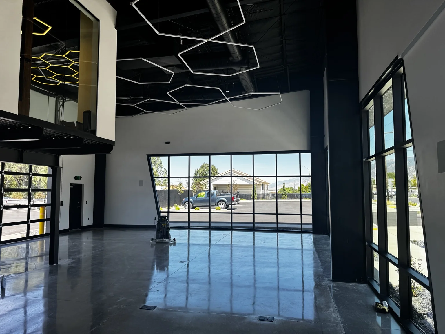 Boat-shop showroom with floor-to-ceiling storefront glass, a reflective polished floor, a black exposed ceiling, and geometric pendant lights